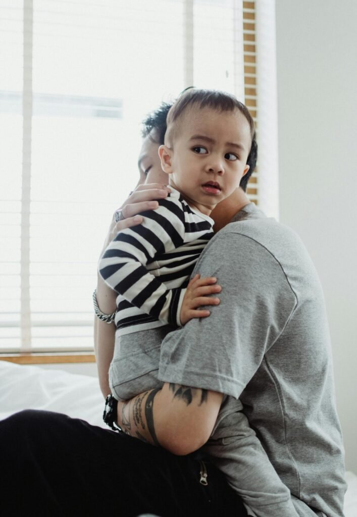 Father holding and comforting his young son by the window, showcasing warmth and family bond.