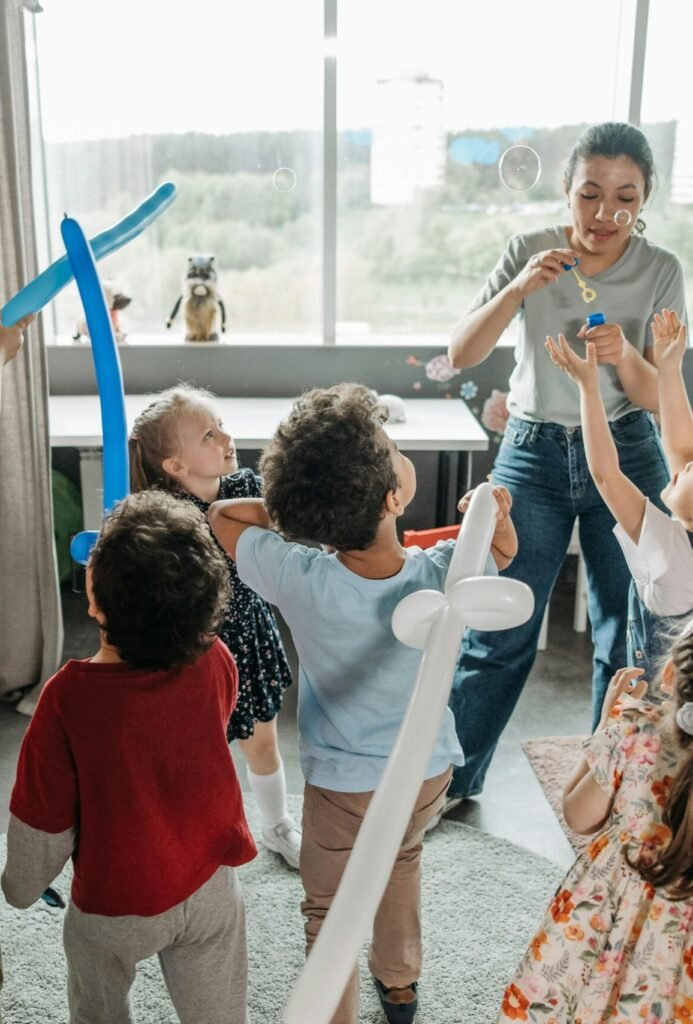 Kids and teachers having fun with bubbles and balloons in a lively classroom setting.